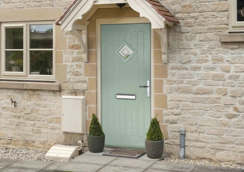 doorco front door. The composite door is green and finished onto a cottage, stone cottage. There is a canopy above the door. The chartwell green door is flanked by two plants on either side. You can see the casement window on either side. 